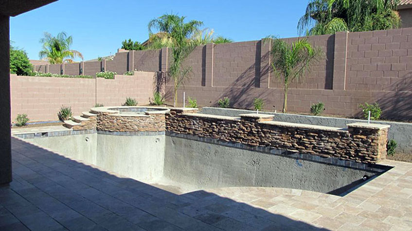 An empty in-ground pool lined with stone walls awaits water and final finishing.