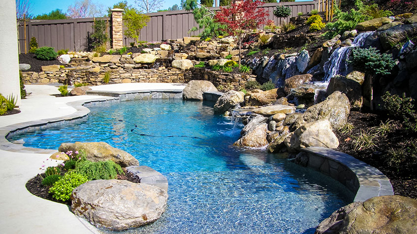 A serene backyard pool surrounded by rocks and cascading waterfalls, creating a tranquil outdoor oasis.