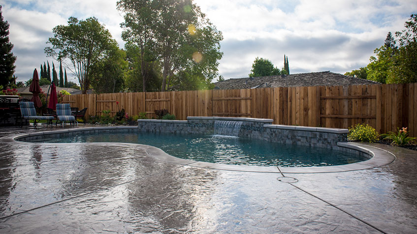 A swimming pool surrounded by a concrete deck and enclosed by a wooden fence.