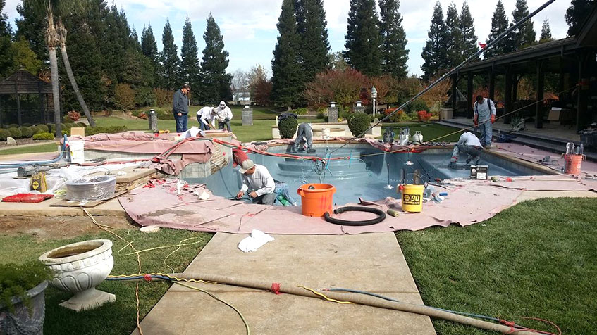 Workers constructing a pool with concrete and other materials, with tools and supplies visible around the site.