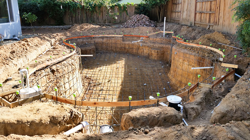 A partially constructed pool with exposed rebar and dirt walls during excavation.