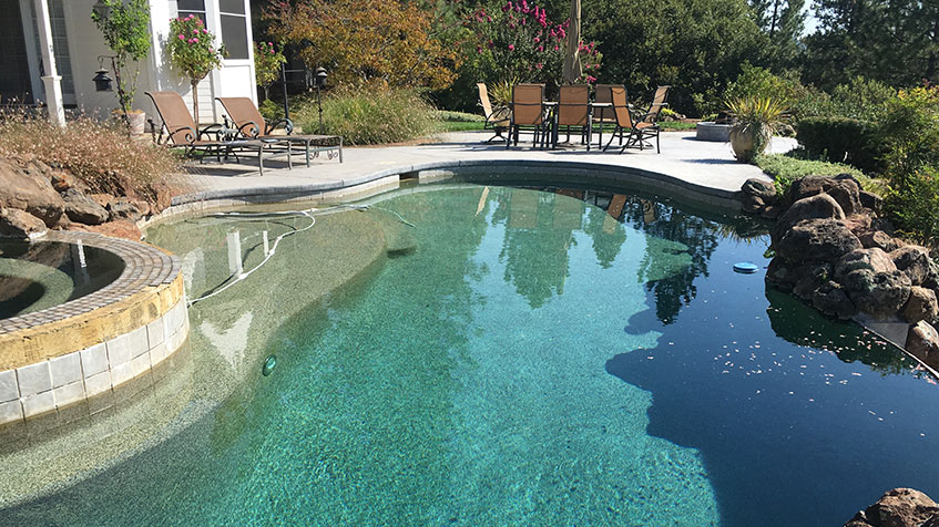 A freeform backyard pool with an attached spa, surrounded by patio seating and landscaping.
