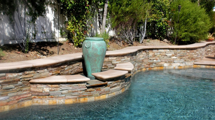 A curved pool features a built-in stone bench and a decorative ceramic urn along a stone retaining wall.