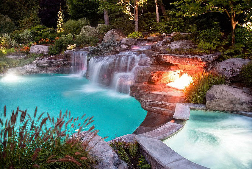 A vibrant, lagoon-style pool with waterfalls glows with colored lighting among lush greenery.