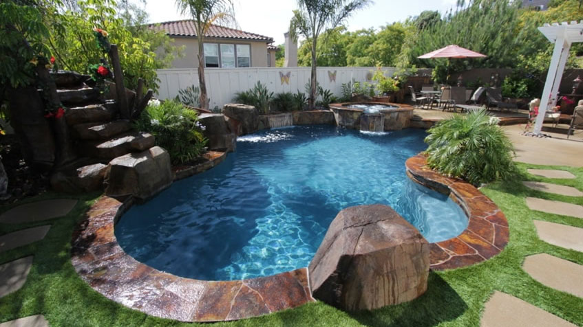 A compact backyard pool with stone accents, lush plants, and a small waterfall feature.