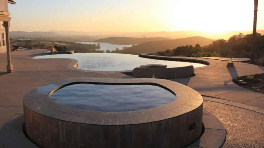 An infinity-edge pool and spa overlook a scenic valley view at sunset.