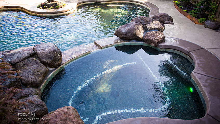 A round, rock-lined spa with underwater lights is connected to a multi-level pool.