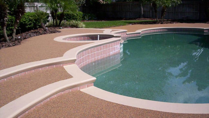 A curved pool with pink tile accents and a small raised spa in a neatly landscaped yard.