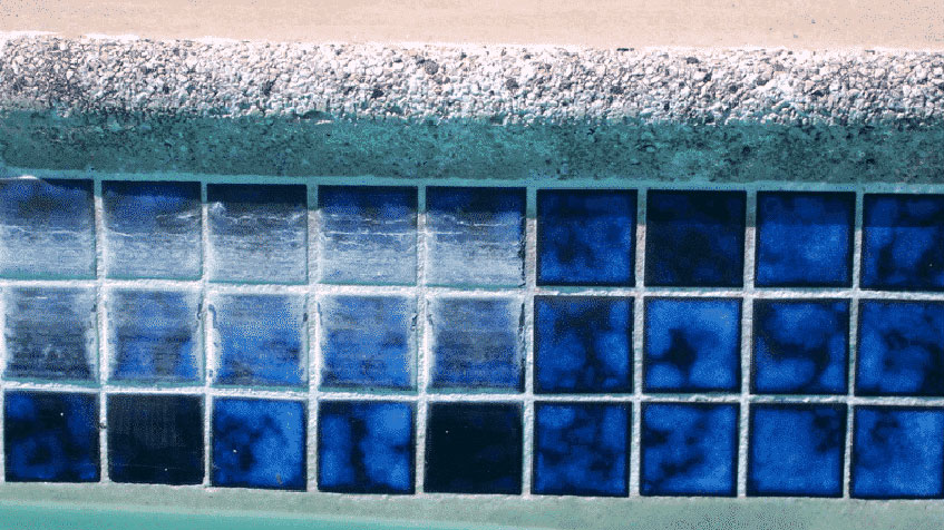 A close-up of blue pool tiles showing calcium buildup along the waterline.