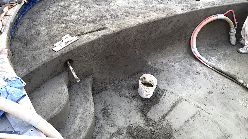 Freshly sprayed concrete forms pool steps and curved walls during gunite construction.