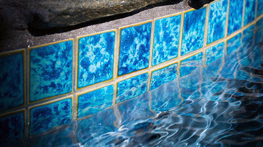Bright blue water reflects against a row of vibrant blue tiles along a pool wall.