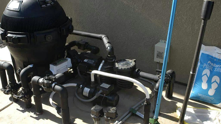A backyard pool pump system with pipes, a filter, and a salt system sits against a stucco wall.