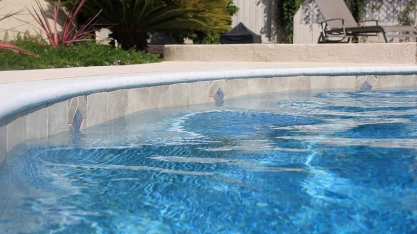 A close-up of a tile-lined pool edge with clear water rippling beneath the coping.