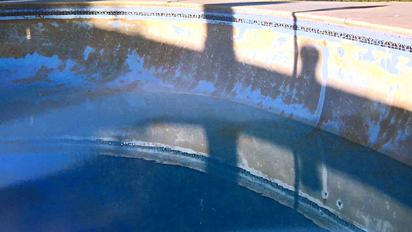 Pool interior showing two underwater bench seats or steps with shadows cast on them, blue tile trim visible at waterline along the pool edge.