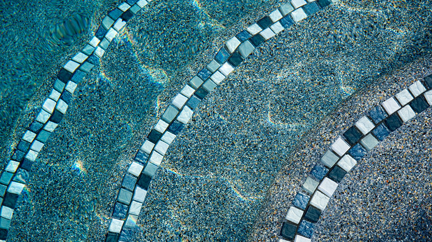 Pool surface showing decorative mosaic tile work with diagonal stripes in alternating shades of blue, teal, and white small square tiles creating a geometric pattern.