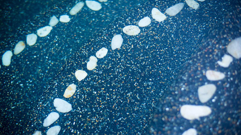Detailed view of blue pool surface with decorative white tile accent stripe running diagonally across the speckled blue pebble finish.