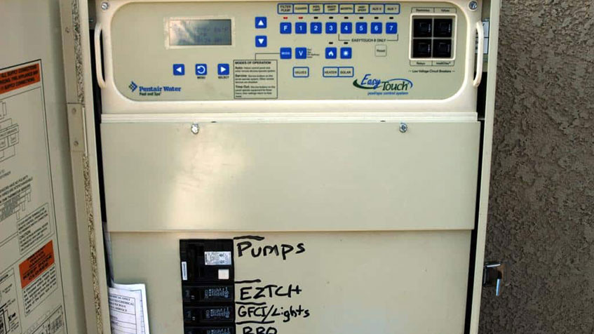 Pool equipment control panel labeled "Pentair Water EasyTouch" with digital display and blue control buttons, handwritten label showing "Pumps EZTCH GFI/Lights RPD" mounted on textured wall.